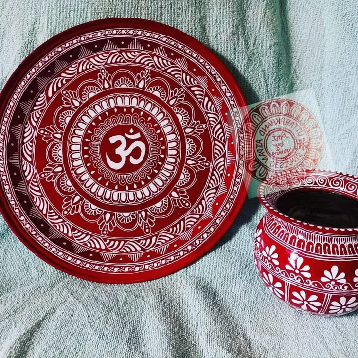 a red and white plate sitting on top of a bed next to a cup