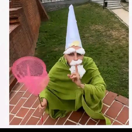 an old man dressed as a gnome holding a pink frisbee in his hand