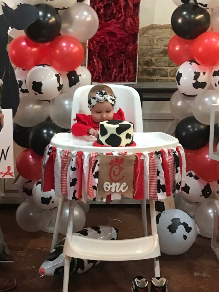 a baby is sitting in a highchair surrounded by balloons and other decorations for a cow themed birthday party