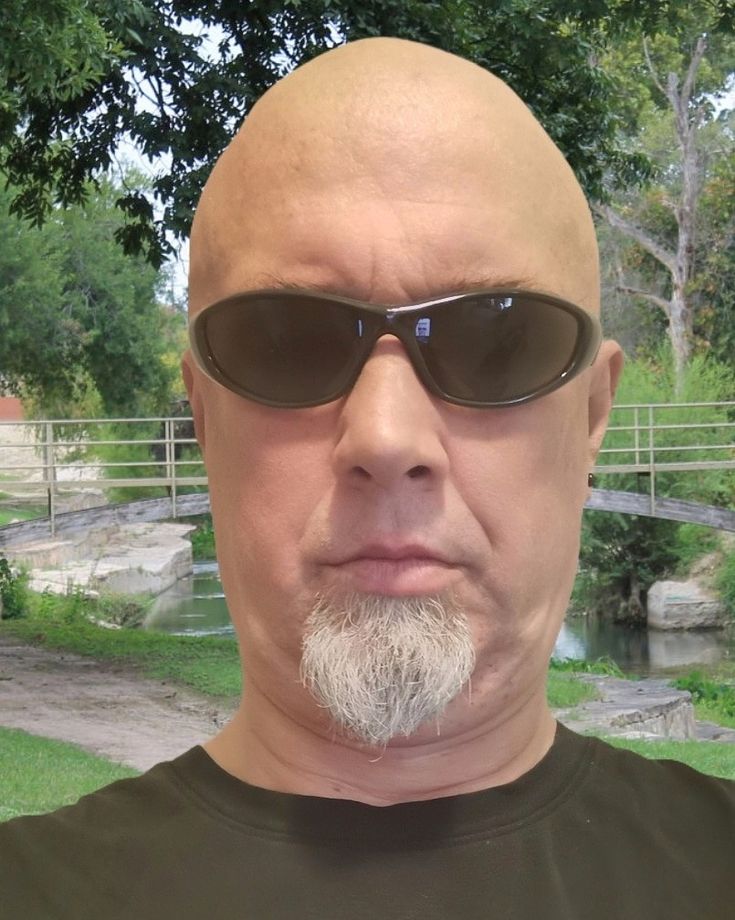 a bald man with sunglasses on his head is looking at the camera while standing in front of a pond