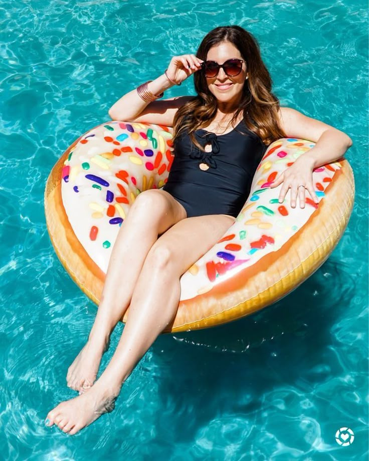 a woman sitting on an inflatable donut float floating in the blue water