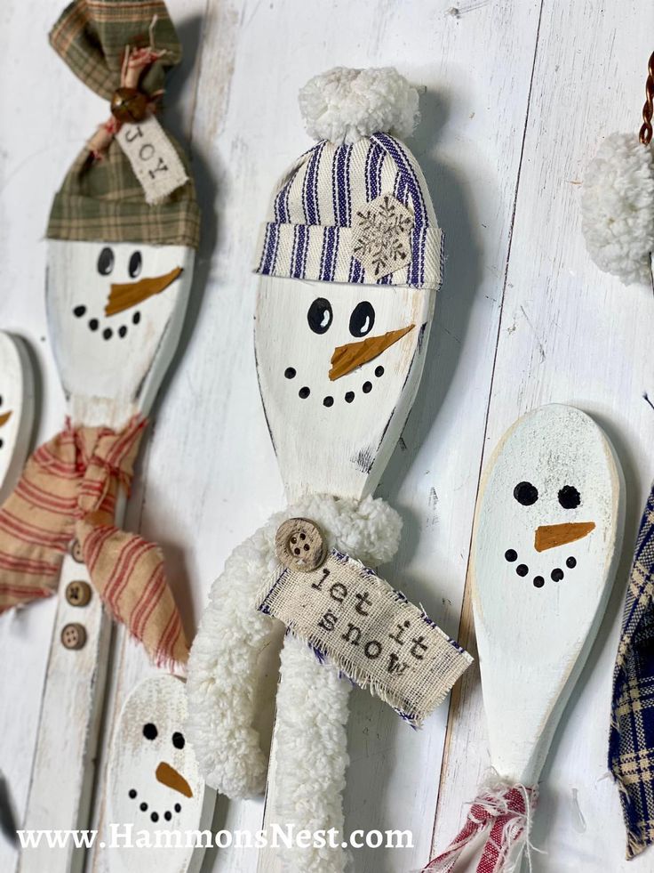 snowman spoons are hanging from hooks on a white wooden wall, decorated with ribbons and tags