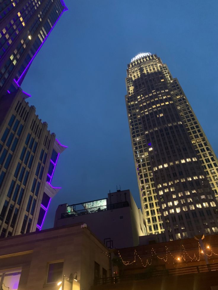 two tall buildings lit up at night with lights in the windows and below them are skyscrapers