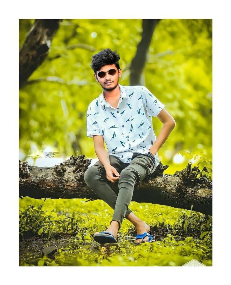 a man sitting on top of a tree branch in the forest wearing red sunglasses and a blue shirt