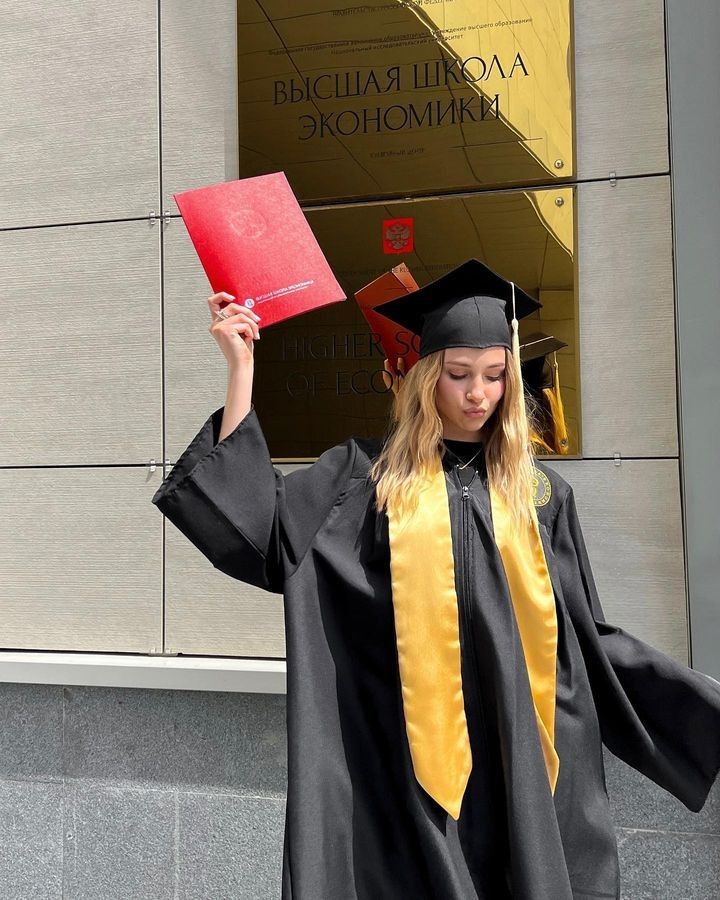 a woman wearing a graduation gown and holding a red book in front of a building