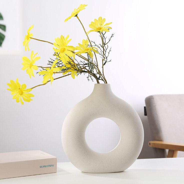 a white vase filled with yellow flowers sitting on top of a table next to a box