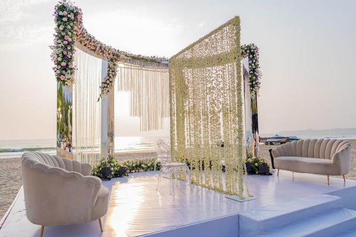 an outdoor ceremony set up on the beach with flowers and greenery draped over it