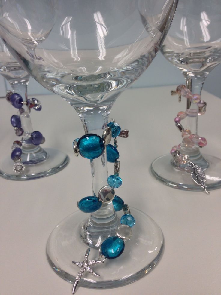 three wine glasses with beads and charms on them sitting on a white table top next to each other