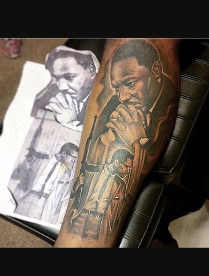 a man with a tattoo on his arm next to a book and some papers in front of him