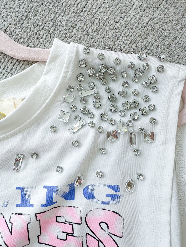 Graphic T-Shirt Cropped Loose Fit Rhinestone Detail On Shoulders Rolling Stones Paired With "Icy Girl" Shorts 95% Cotton 5% Spandex Casual Party Tops With Rhinestones, Casual White T-shirt With Rhinestones, Casual Pink Tops With Rhinestones, Spring Stretch Tops With Rhinestones, Casual Pink Embellished Tops, Spring Pink Rhinestone Tops, Stretch Crew Neck Top With Rhinestones, White Embellished Cotton Tops, White Rhinestone Crew Neck Top