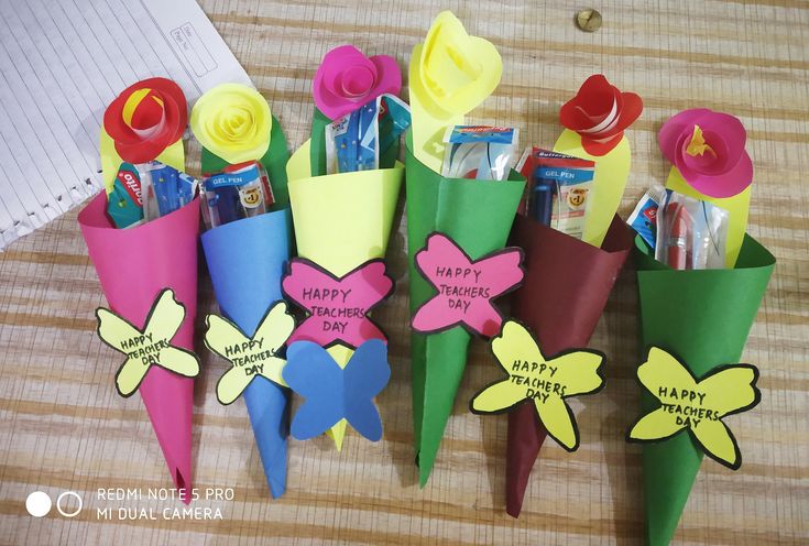 some paper flowers are sitting on a table with pens and pencils in each one