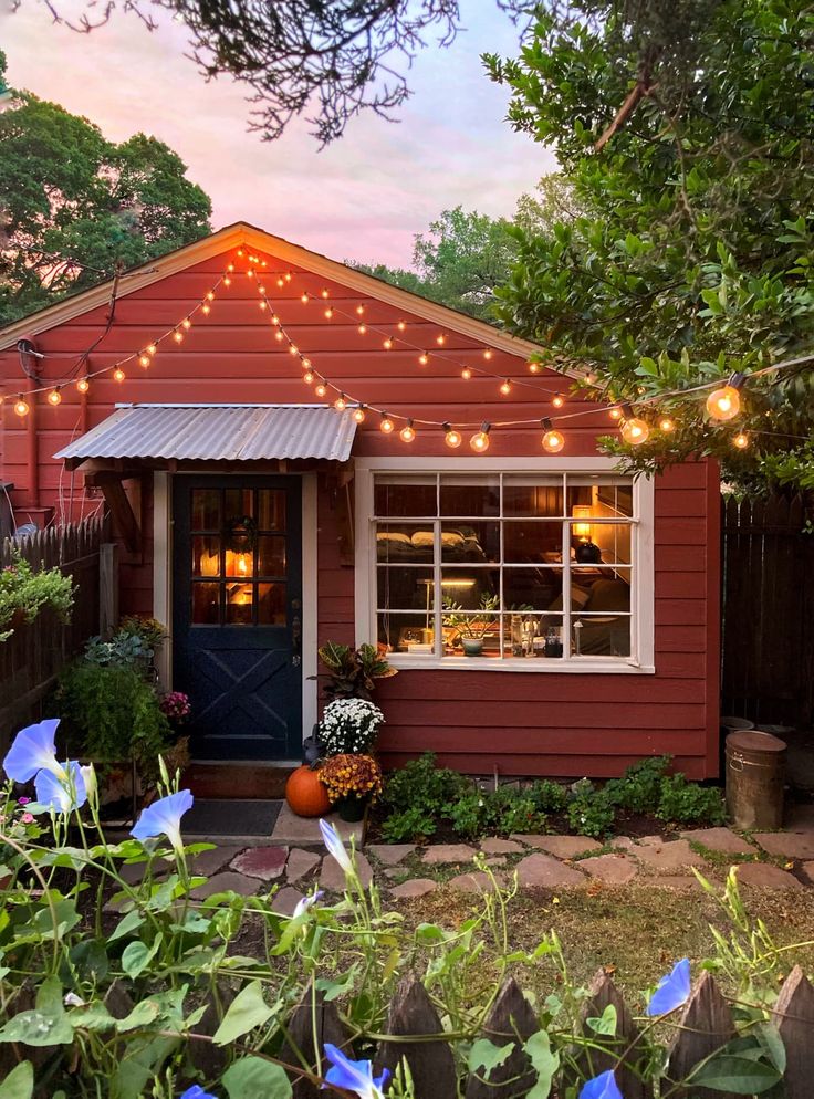 a small red house with lights on the roof and flowers in pots around the front door