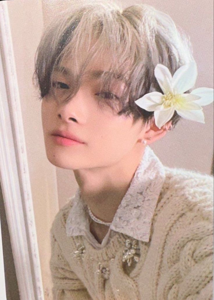 a young man with a flower in his hair looking at the camera while wearing a sweater