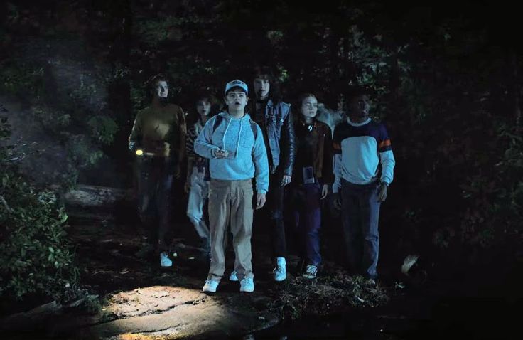 a group of people standing next to each other in the woods at night with lights on