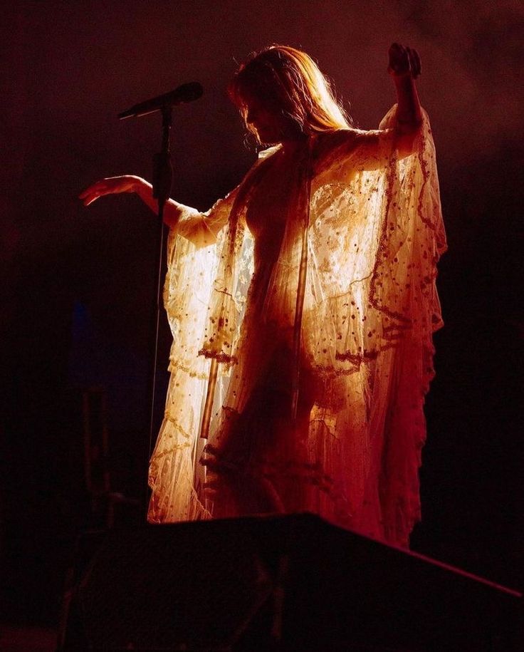 a woman with long hair standing in front of a microphone and holding her hands up