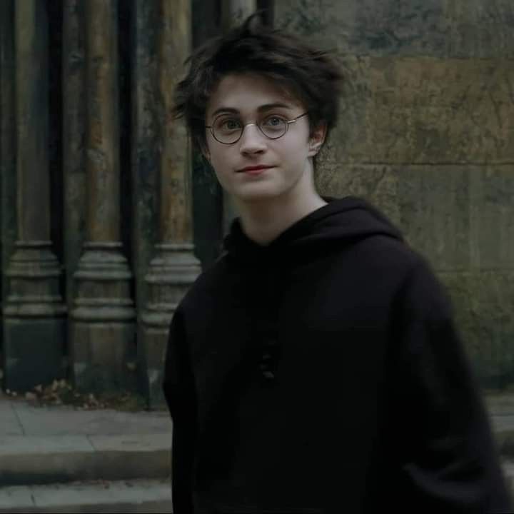 a young man with glasses standing in front of a stone building and looking at the camera