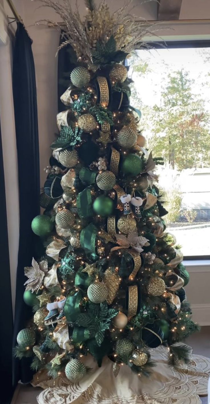 a decorated christmas tree with green and gold ornaments on it in front of a window