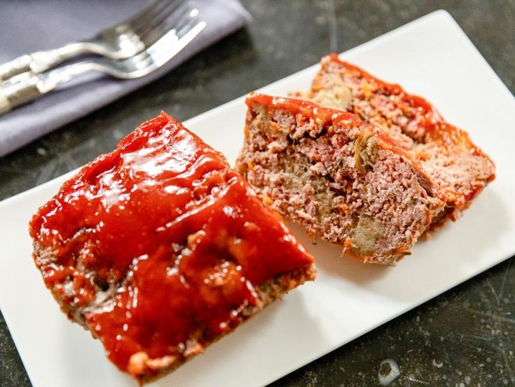 two slices of meatloaf on a white plate next to a fork and knife