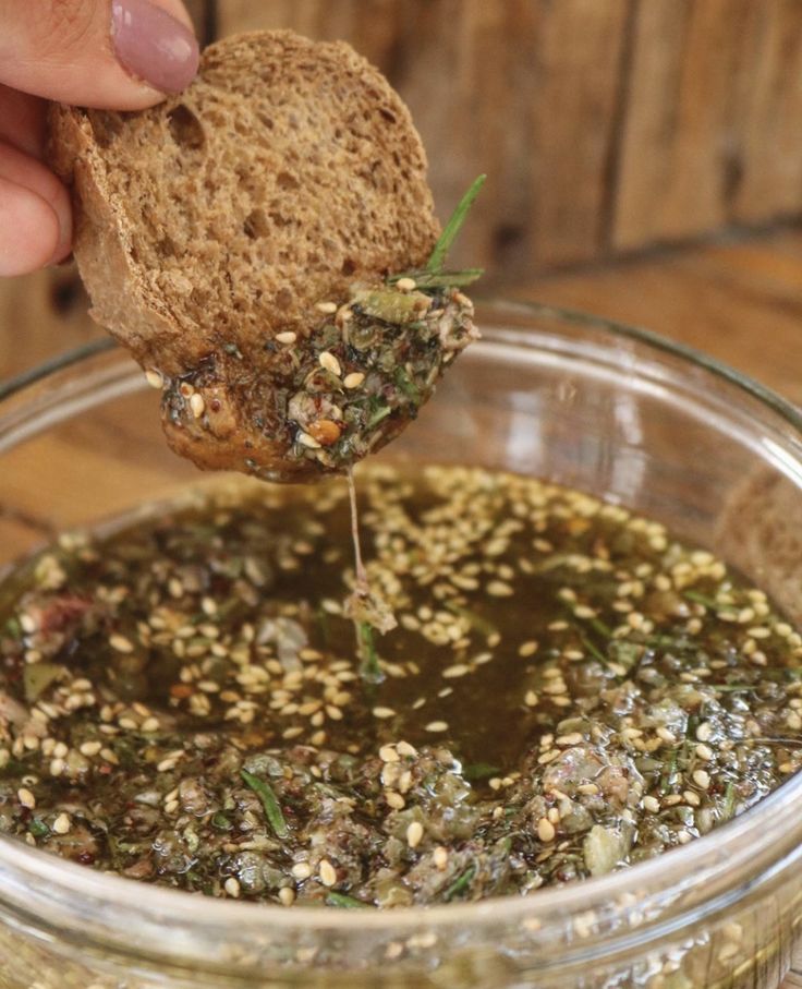 a person dipping something into a glass bowl filled with pesto, bread and sprouts