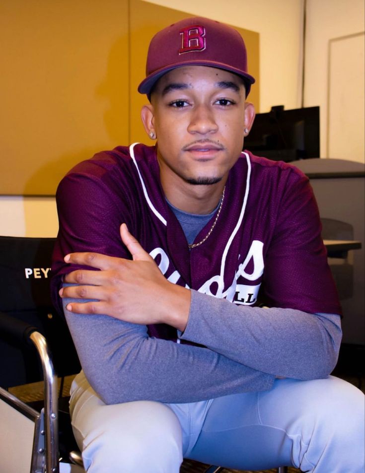 a baseball player sitting in a chair with his arms crossed and looking at the camera