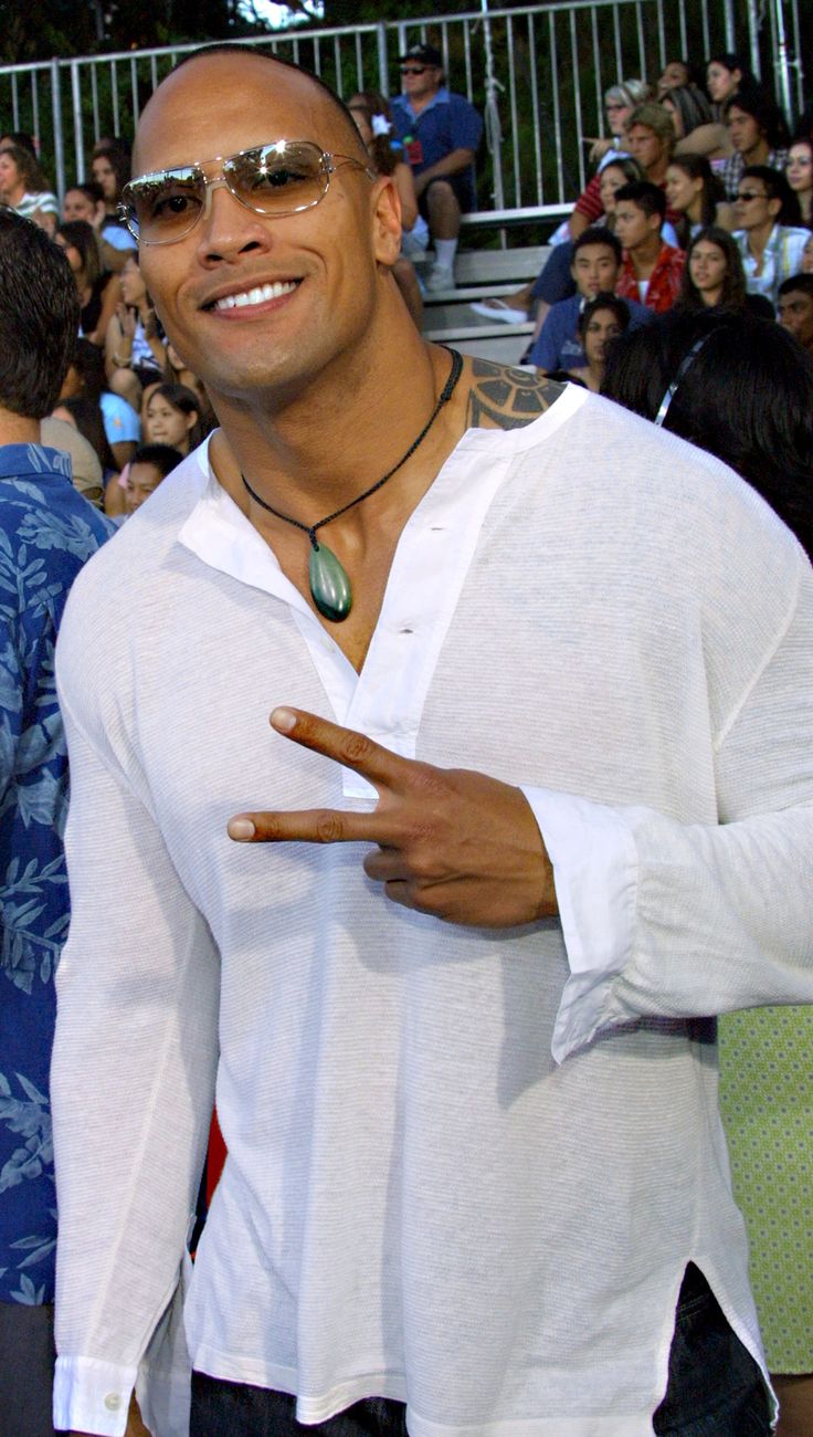 a man in white shirt and sunglasses pointing to the side while people watch from behind him