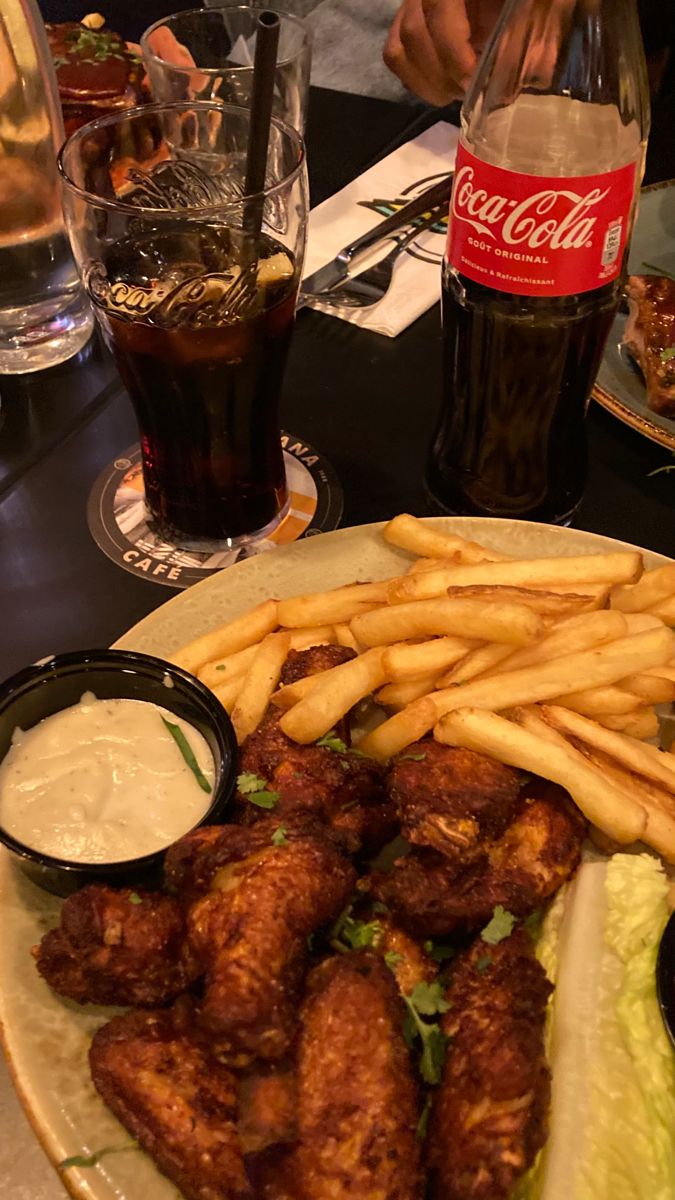 chicken wings and french fries are served on a plate with coleslaw, ketchup, and soda