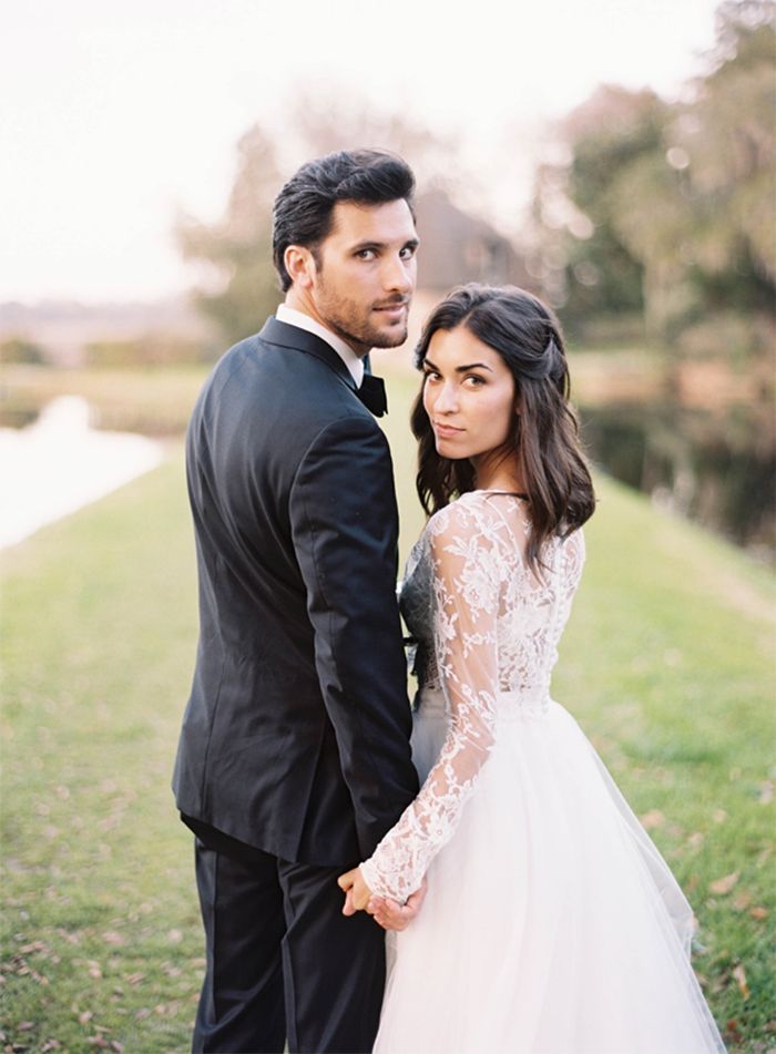 a bride and groom standing next to each other in front of a pond wearing tuxedos