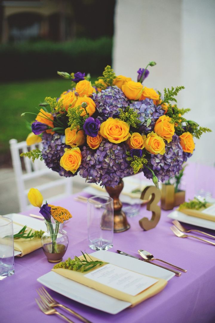 the table is set with yellow and purple flowers in vases, napkins, and silverware