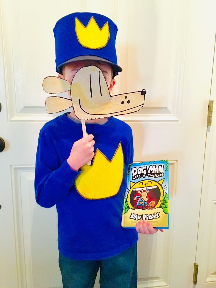 a young boy wearing a blue shirt and hat holding a book while standing in front of a door