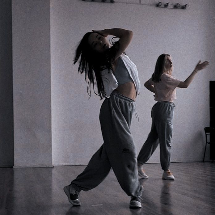 two young women are dancing in a dance studio, one is wearing sweatpants and the other has long hair