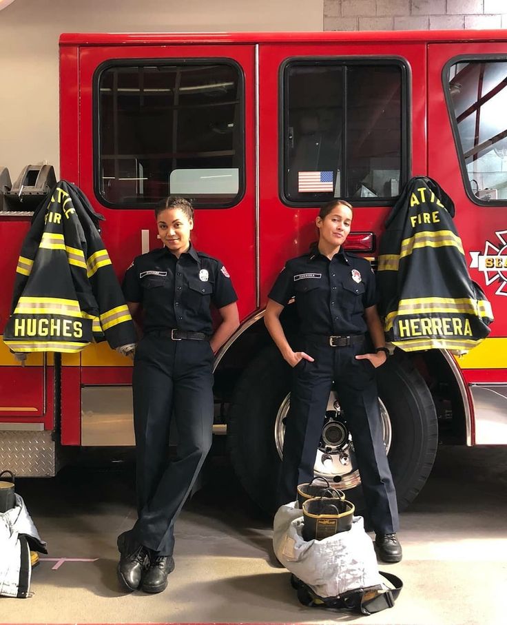 two women in uniform standing next to a fire truck