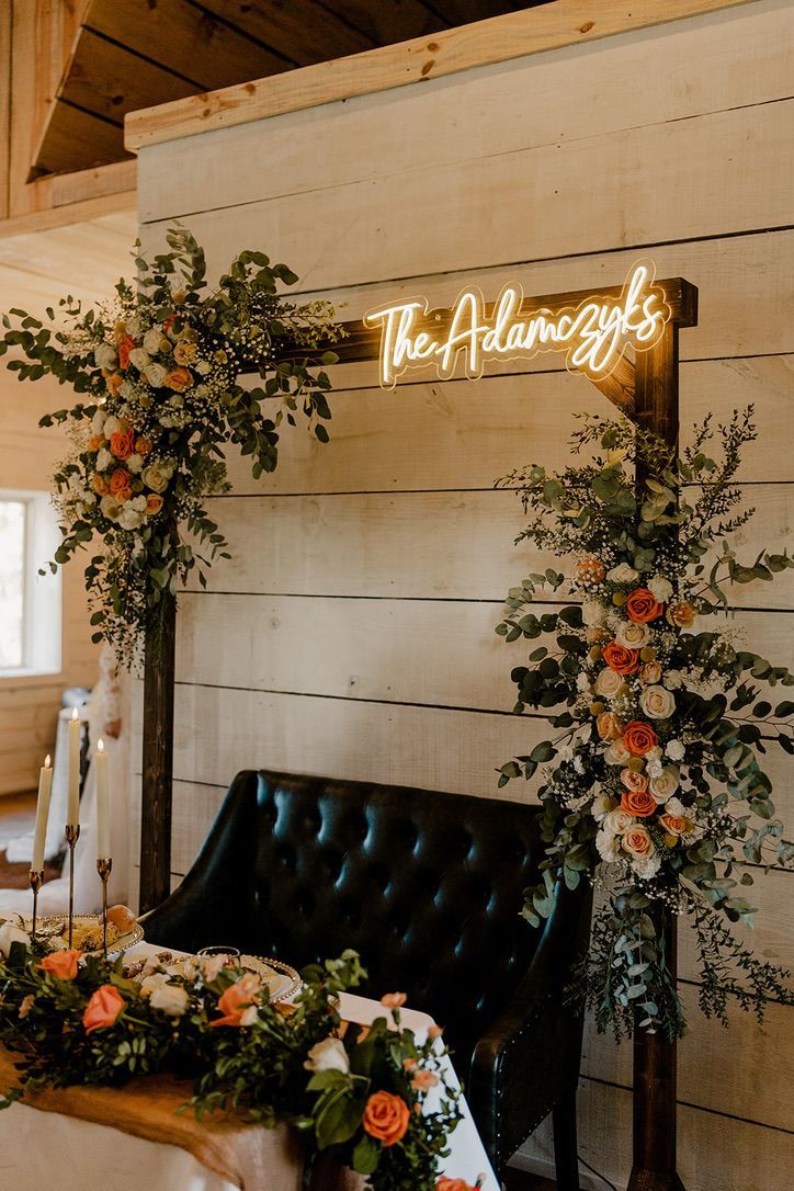 a table with flowers and greenery under a neon sign