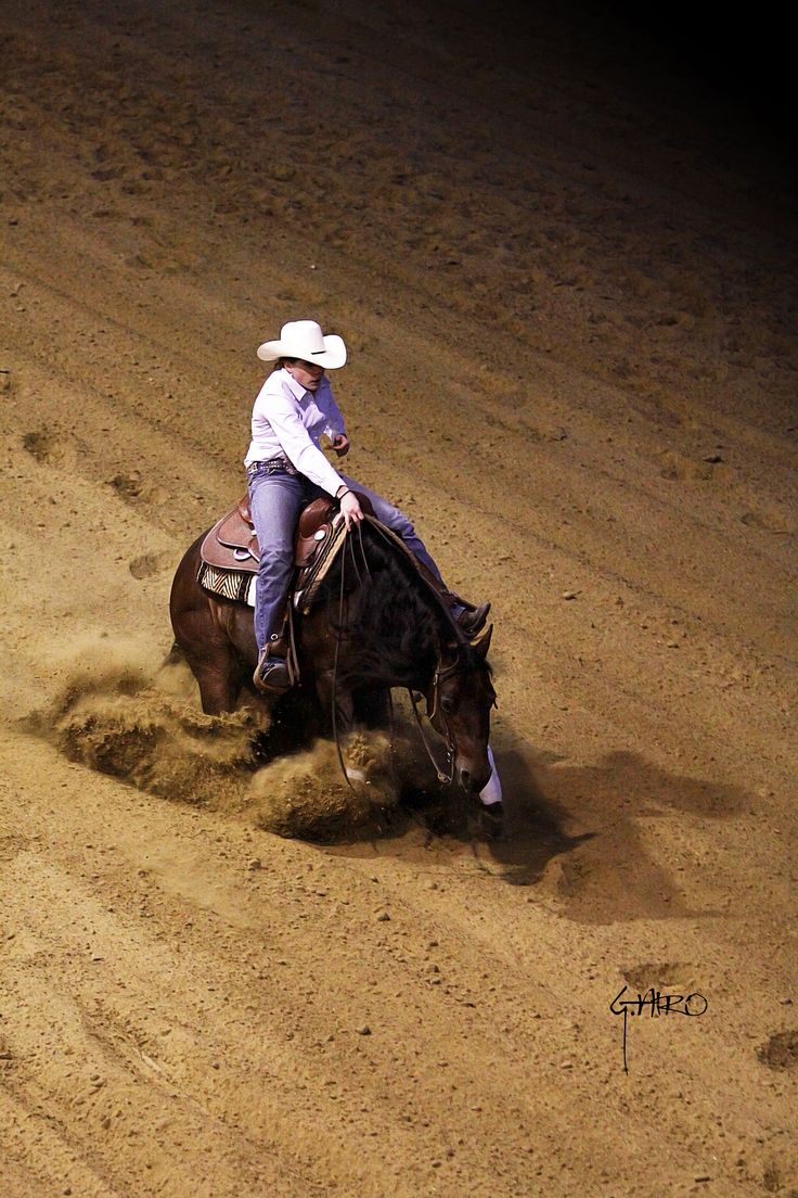 a man riding on the back of a brown horse in an arena covered in dirt