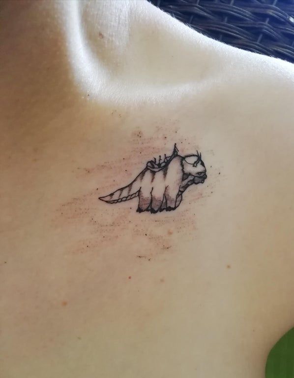 a small tattoo on the back of a woman's upper body, with an image of a dinosaur