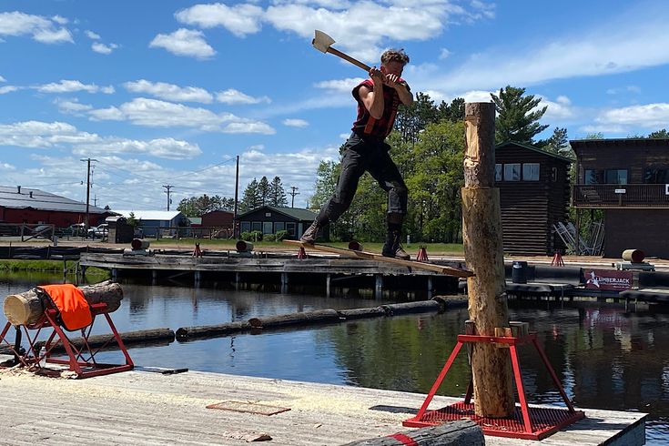 a man walking across a wooden bridge over water with an axg in his hand