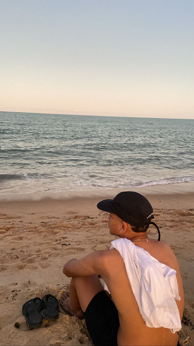 a person sitting on the beach with their feet in the sand looking at the water