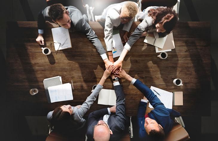 four people sitting at a table with their hands together