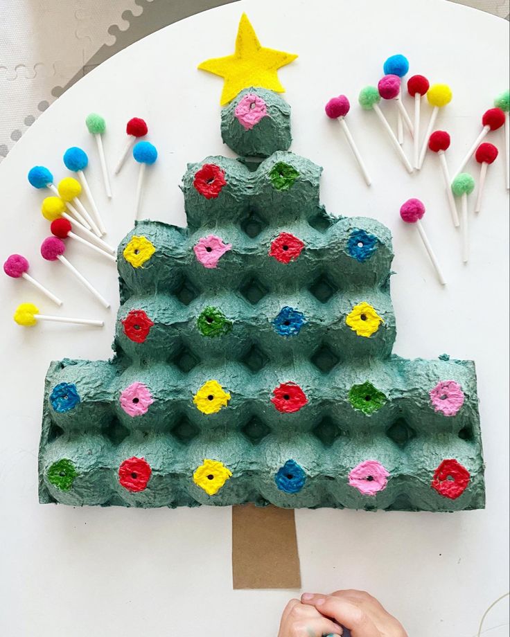 a child's hand holding a piece of paper next to a christmas tree made out of egg cartons