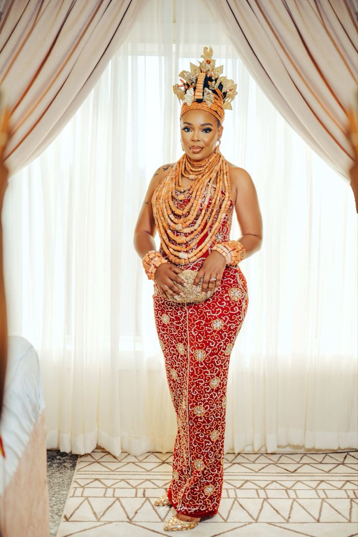 a woman in a red and gold outfit standing next to a window with sheer drapes