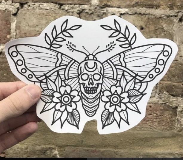 a hand holding up a sticker with a skull and butterfly design on the back