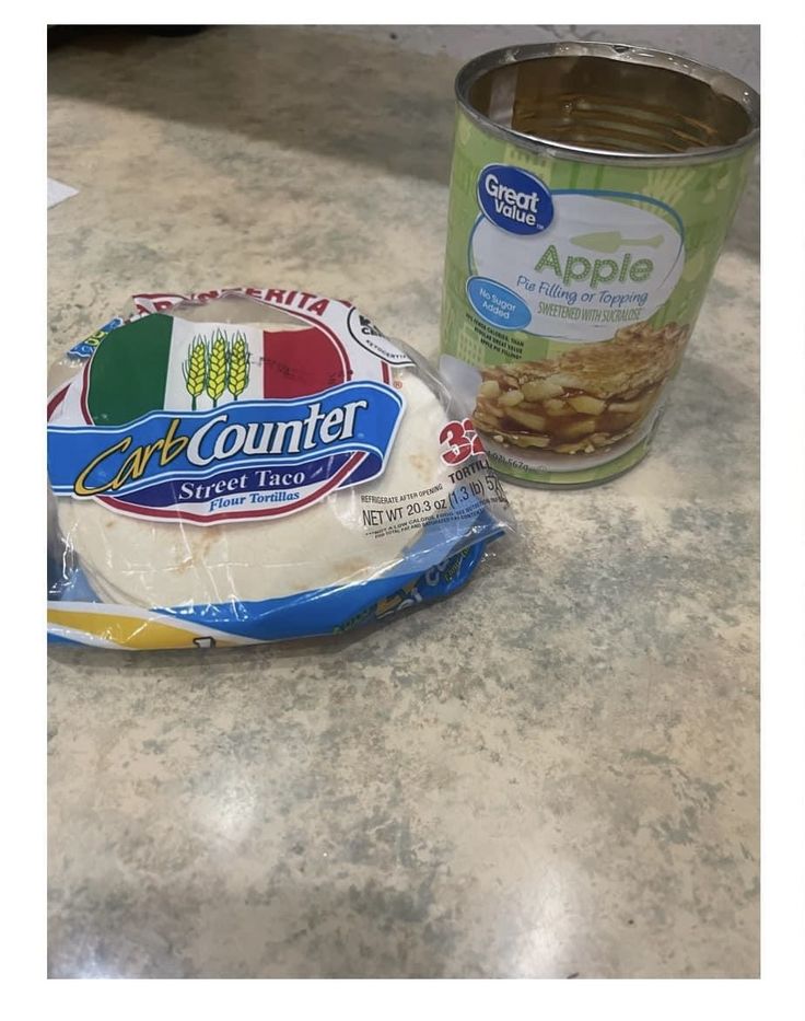 a can of yogurt and some kind of food on a counter top next to an apple