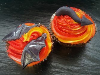 two cupcakes with orange and red frosting on them sitting on a black surface