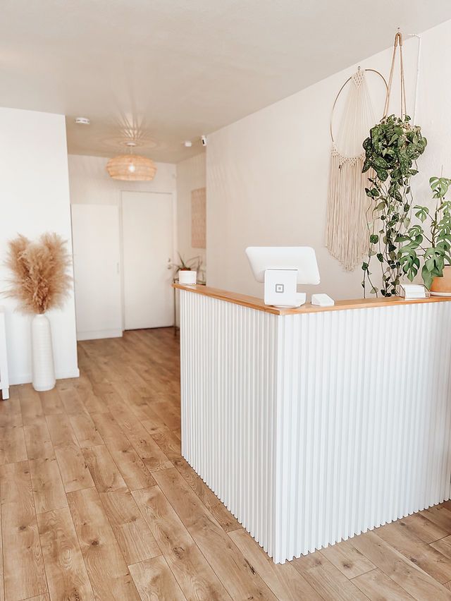 a white reception desk in an office with wood flooring and potted plants on the counter