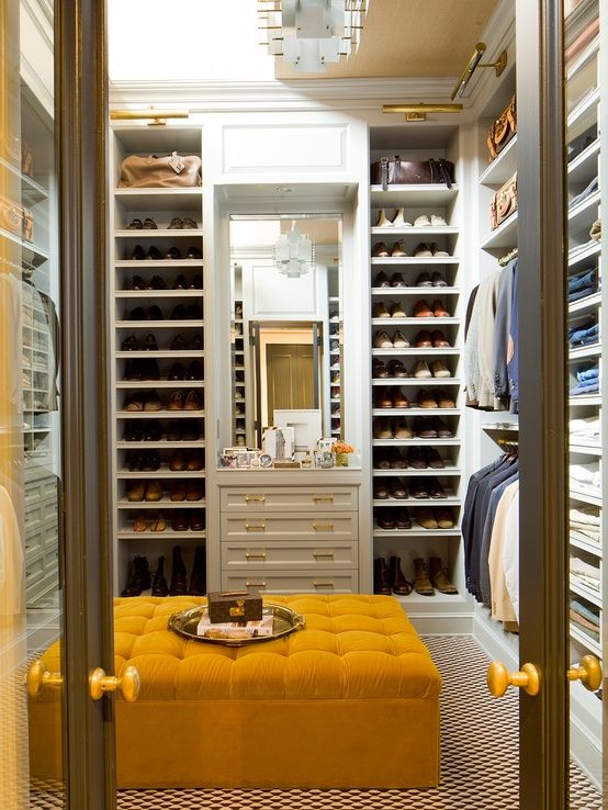 a walk - in closet with yellow foot stool and shelves full of shoes on the floor