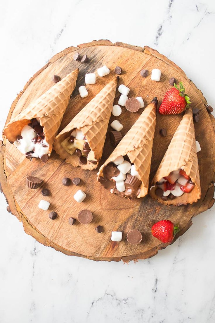 four ice cream cones with strawberries and marshmallows on a wooden board