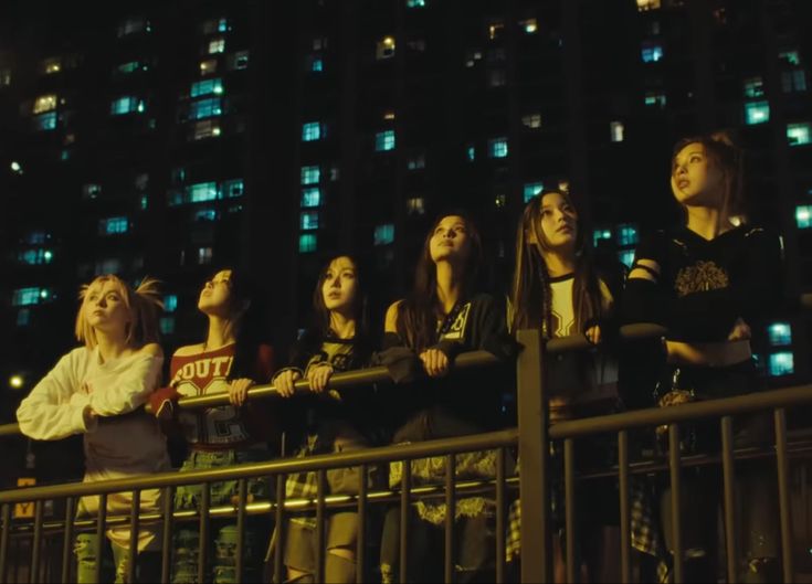 a group of young people standing next to each other on a balcony in front of a tall building