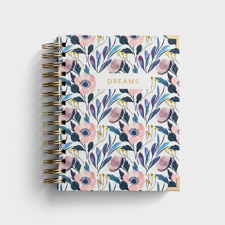 a spiral notebook with flowers and the words dreams written in gold foil on it, against a white background