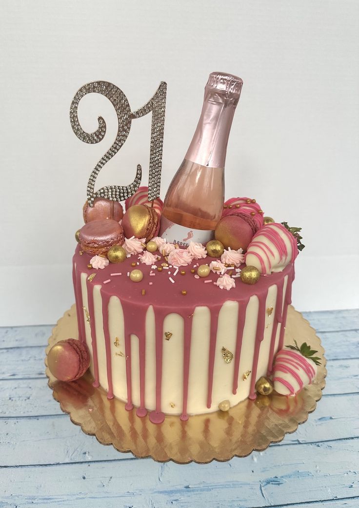 a birthday cake decorated with pink and white icing, gold decorations and a bottle of champagne