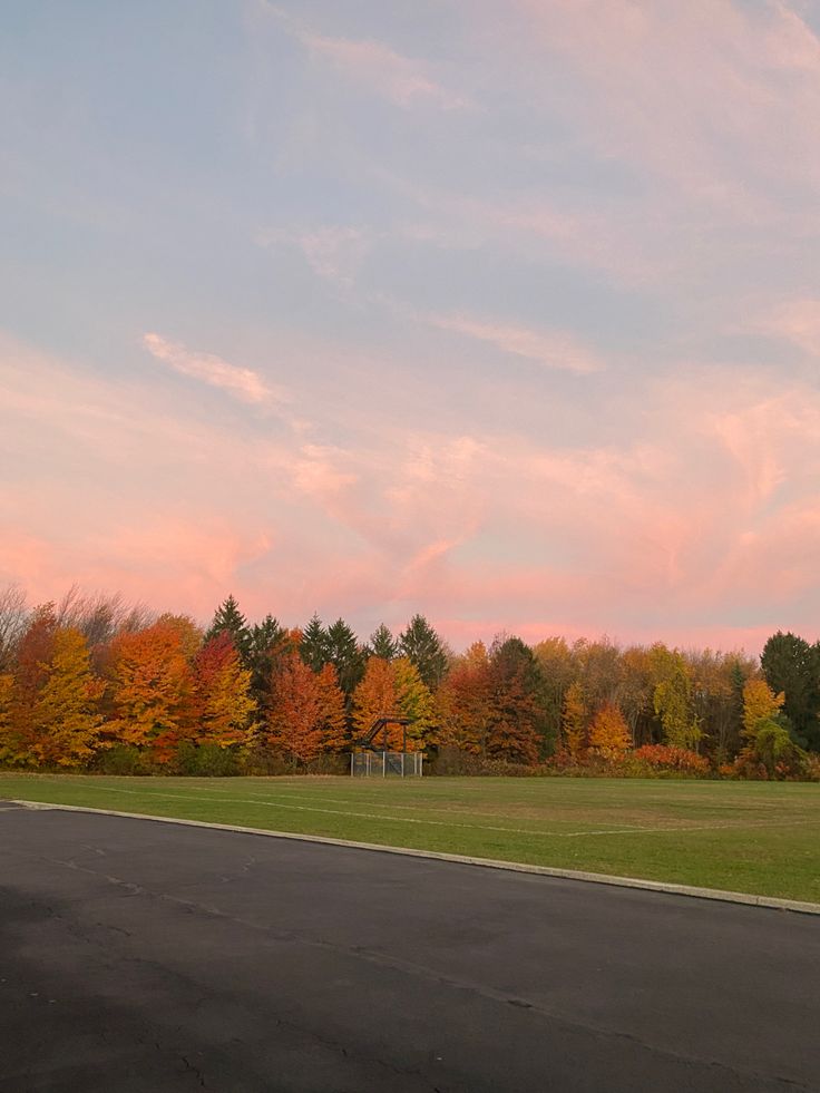 an empty parking lot in front of trees with orange and yellow leaves on the ground