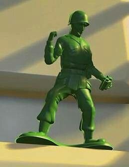 a green toy soldier standing on top of a skateboard in front of a white wall